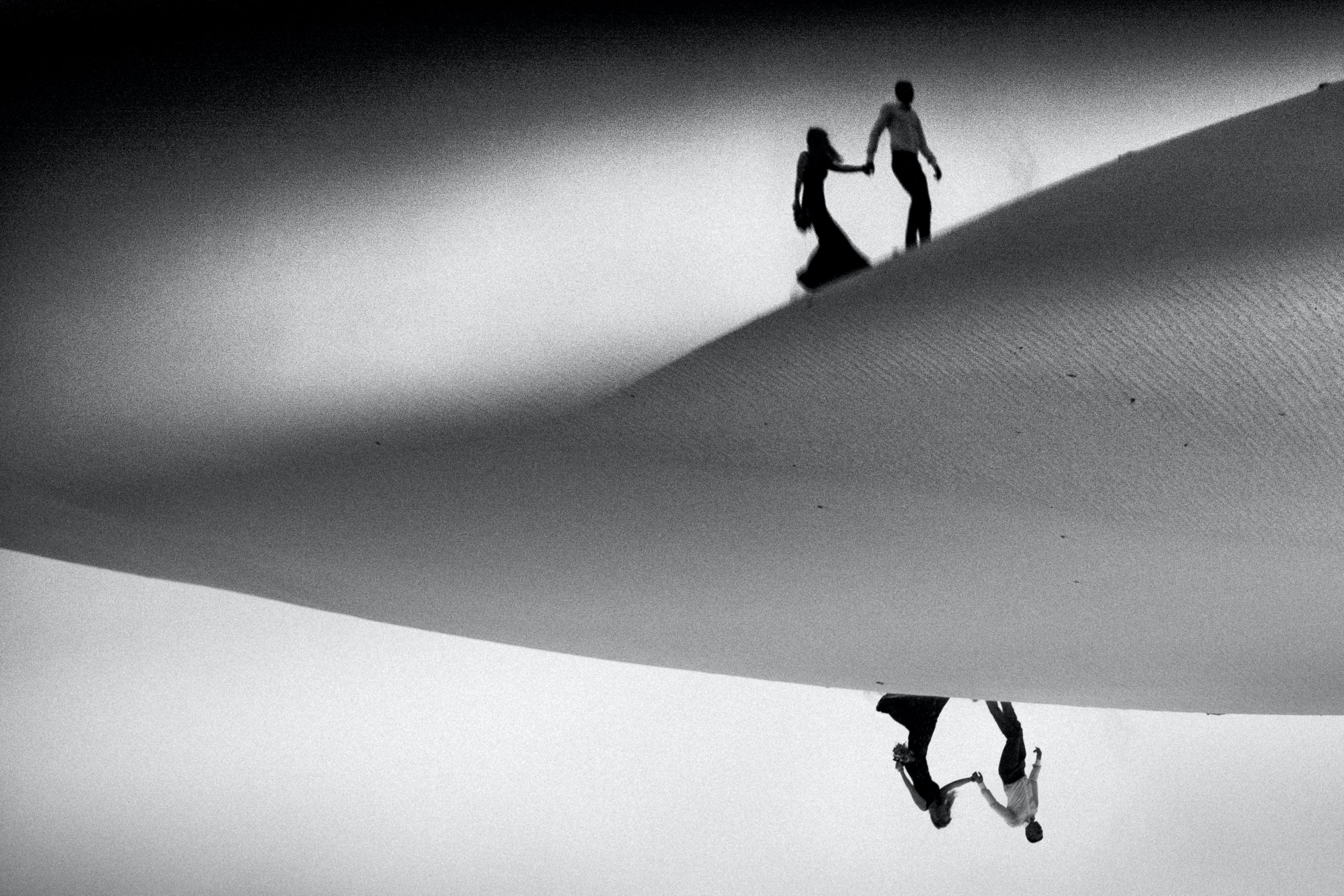 Man leading a woman across a desert sand dune